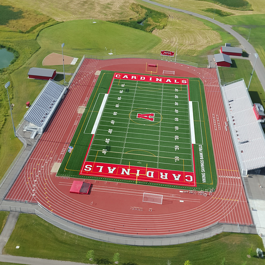 Aerial view of a football field and track with "CARDINALS" in large letters in both end zones. The field, perfect for live sports, is surrounded by bleachers, buildings, and grassy areas.