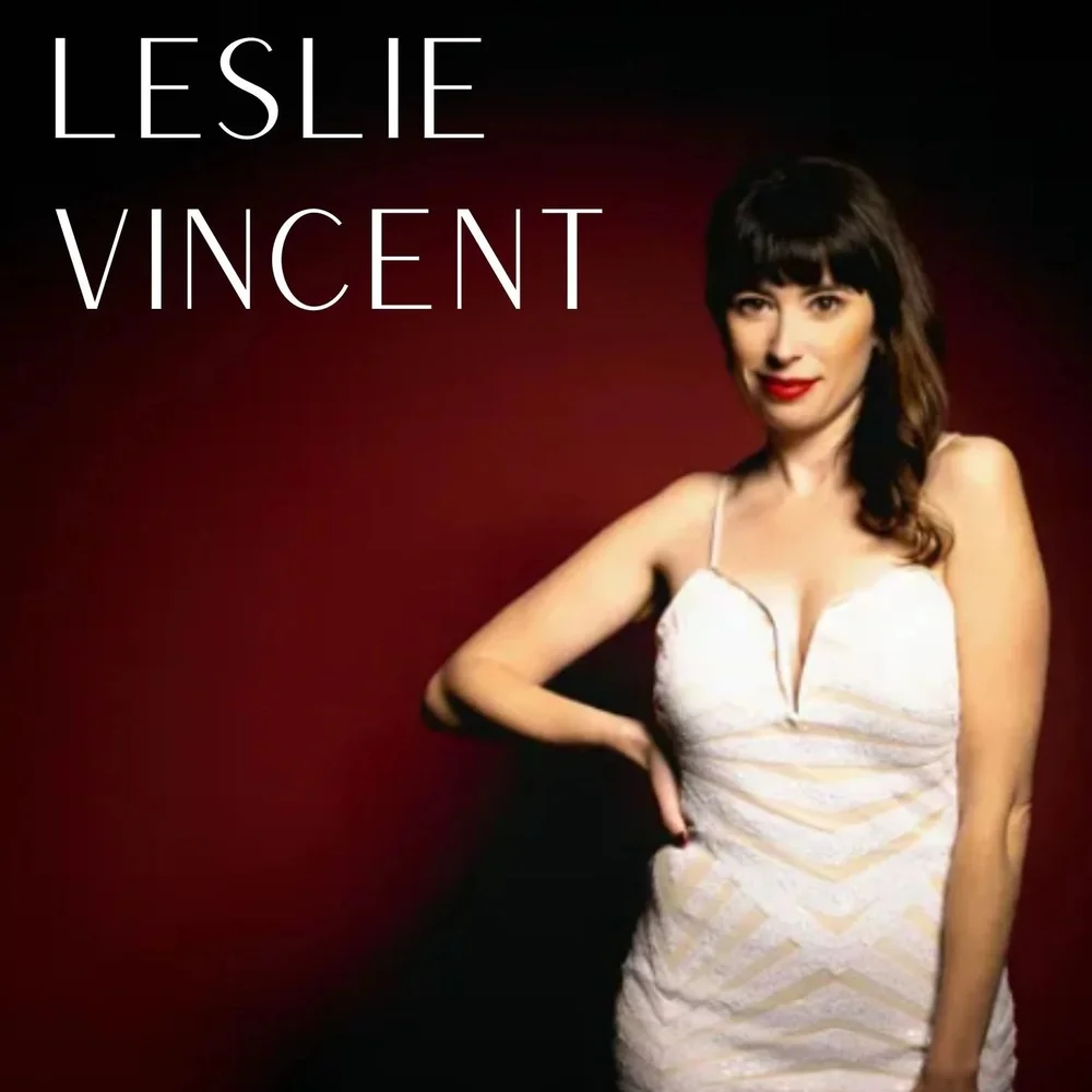A woman in a white dress with wavy dark hair stands against a dark red background, capturing the spirit of live performance. "LESLIE VINCENT" appears in large white letters in the top left corner, evoking the magic of Theatre L'Homme Dieu.