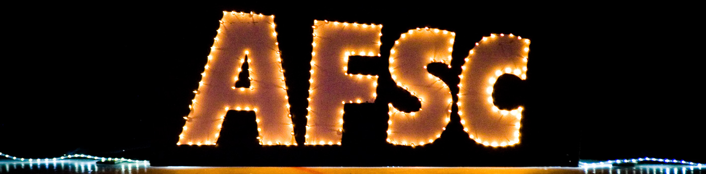 Large letters "AFSC" outlined with bright string lights stand against a dark background, capturing the excitement of the Annual Spring Ice Review, with additional lights glowing at the bottom edges of the image.
