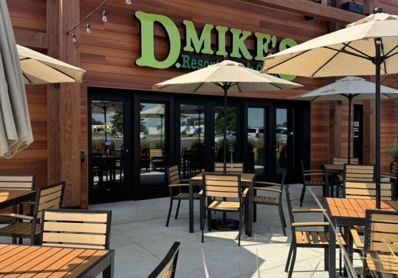 Outdoor patio of D. Mike’s Resort Bar & Grill, featuring wooden tables and chairs with umbrellas. The building’s wooden exterior and string lights overhead create a welcoming, casual dining atmosphere.