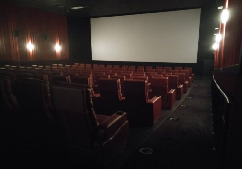 A dimly lit Cinema 9 theater with rows of empty red leather seats faces a large blank screen, softly illuminated by wall lights along the side walls.